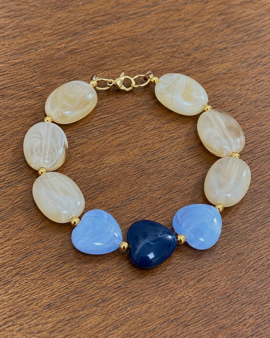 Bracelet à perles ivoire et cœurs bleus porté au poignet — création Lolita, Glaia Collection, Guer