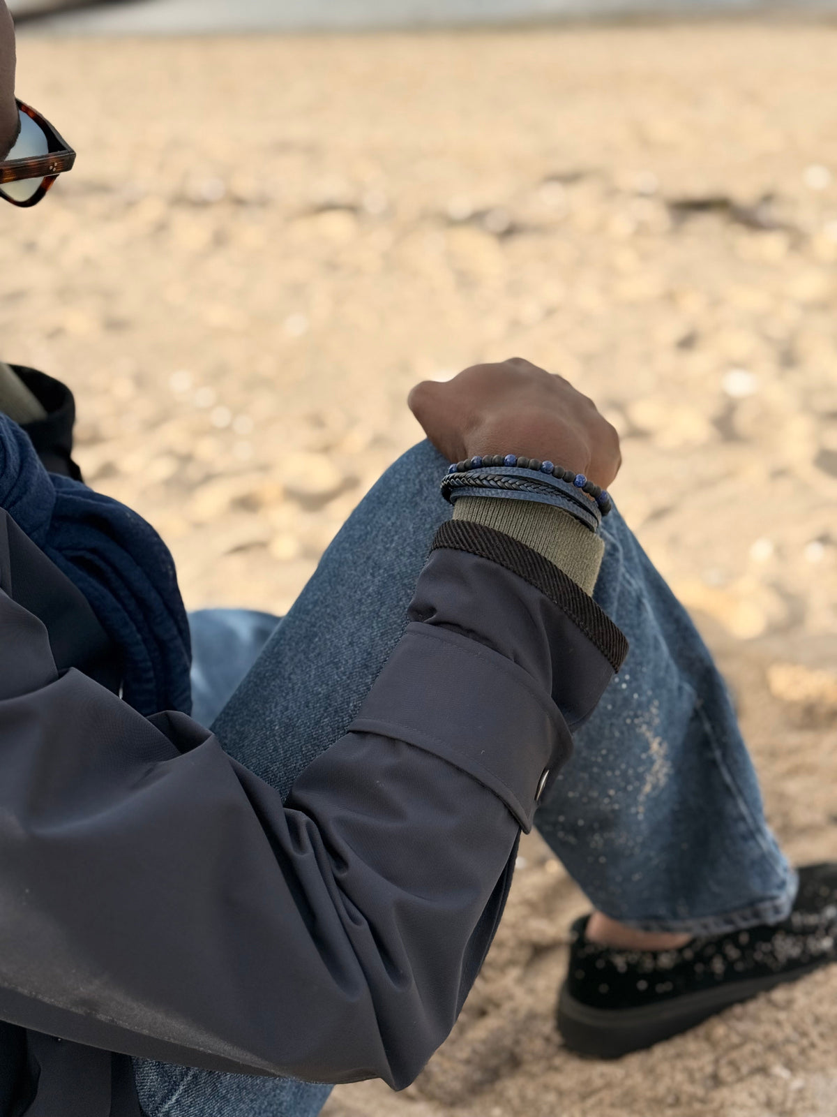 Bracelet homme multi-rangs — perles bleu nuit, tresse de cuir noir et lien plat gris, porté au poignet — Glaia Collection, Guer
