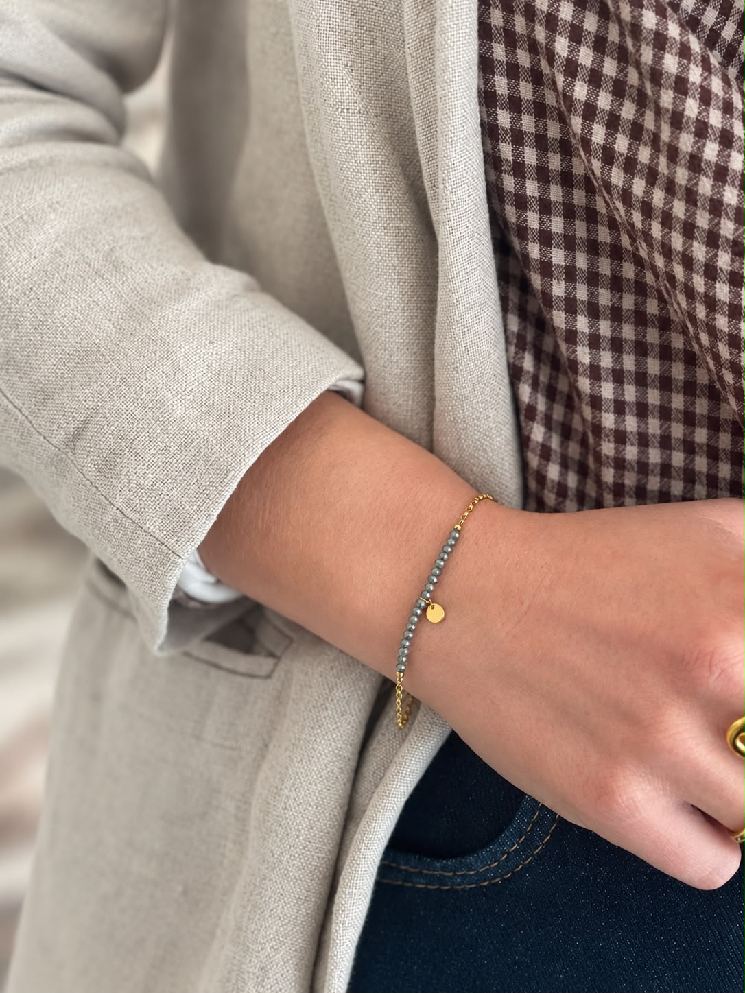 Bracelet à rang de perles et pastille dorée, porté au poignet — Glaia Collection, Guer