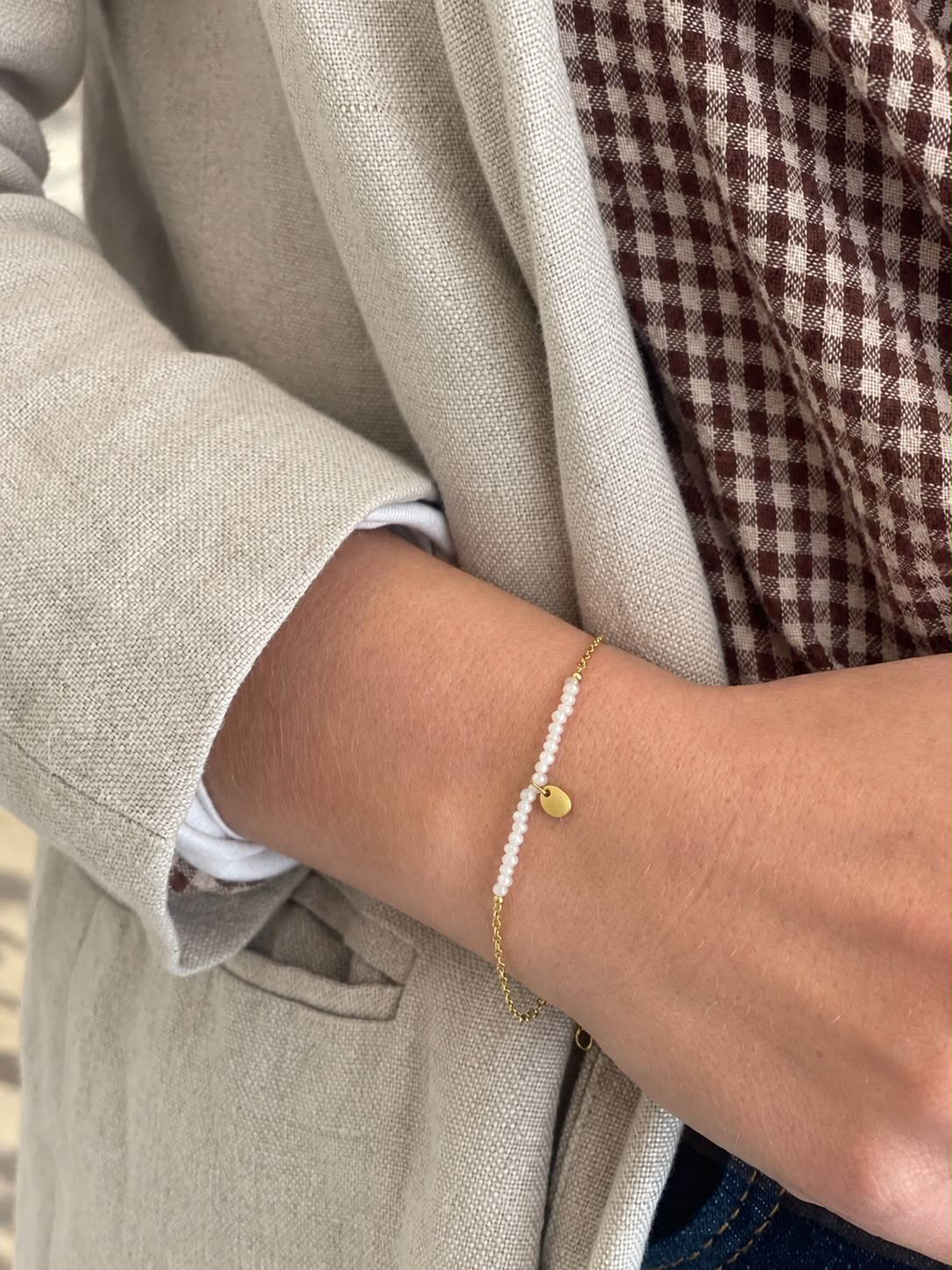 Bracelet à rang de perles et pastille dorée, porté au poignet — Glaia Collection, Guer